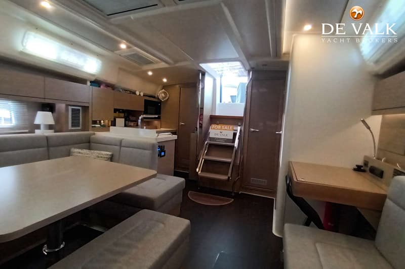 De foto toont het interieur van een boot met een zithoek, tafel, keukenblok, trap naar het dek en een bureau. — Hanse 458