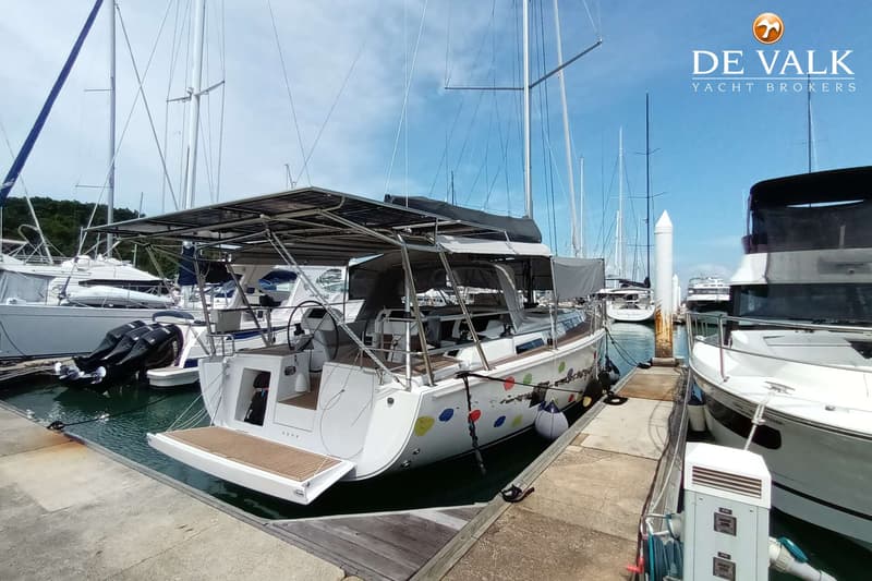 Een witte zeilboot met kleurrijke stippen en een uitklapbaar zwemplateau ligt aangemeerd aan een steiger. — Hanse 458