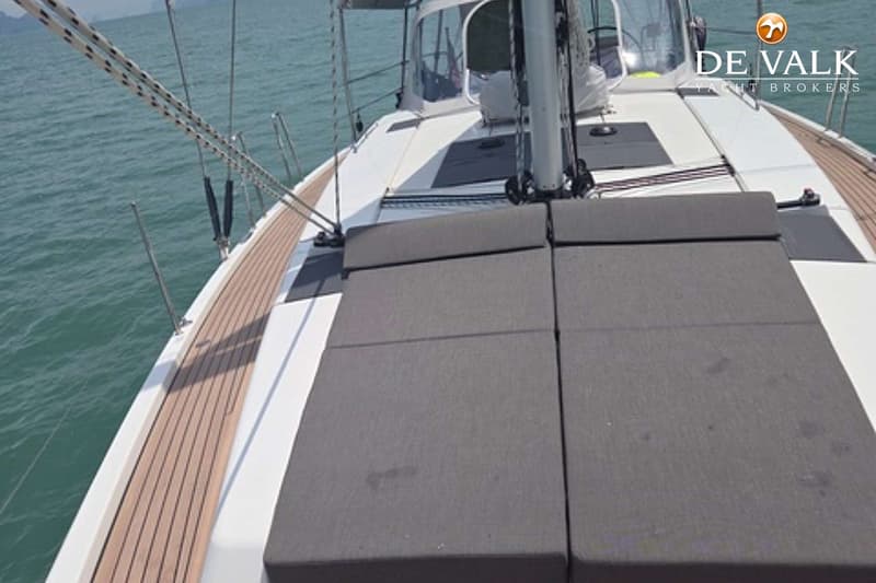 Een bovenaanzicht van een boot met een wit dek, een houten gangboord en grijze kussens. — Hanse 458