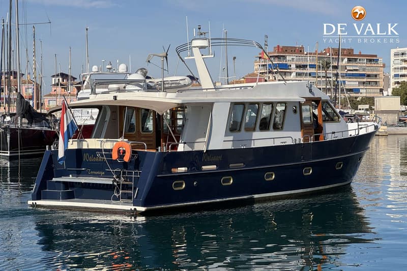 Een donkerblauwe motorboot met witte opbouw en houten details ligt in het water, met gebouwen op de achtergrond.