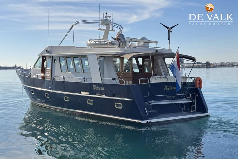 Een donkerblauwe motorboot met een witte opbouw en een Nederlandse vlag, drijvend op rustig water onder een blauwe lucht.