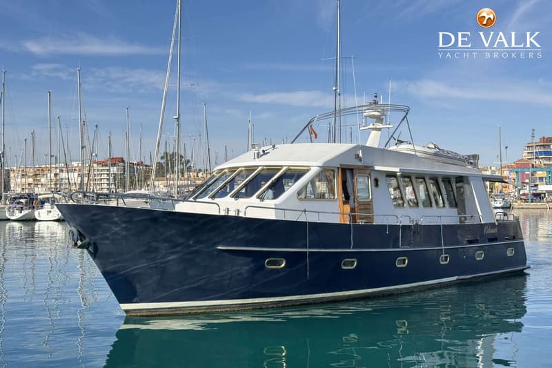 Een donkerblauwe motorboot met een witte opbouw ligt in een haven, omringd door andere boten en gebouwen. — Eurotrawler 1750
