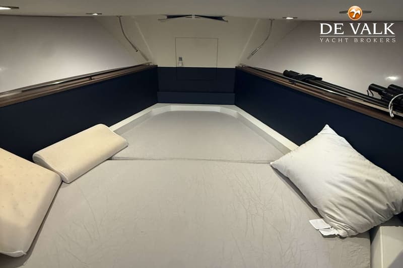 De foto toont een kajuit met een V-vormig bed, twee kussens en donkerblauwe zijpanelen met houten accenten. — Mimi 9,5 WA