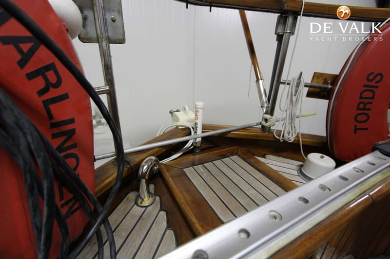 Een detailfoto van een houten bootdek met teak en mahonie, met een rode reddingsboei en een GPS-antenne.