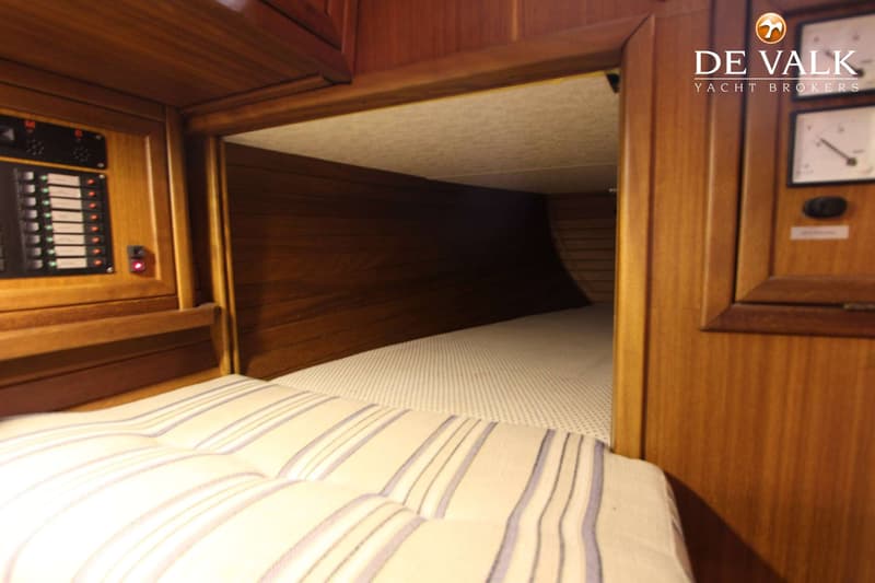 Een houten interieur met een bed met gestreepte kussens en een open doorgang naar een slaapruimte.