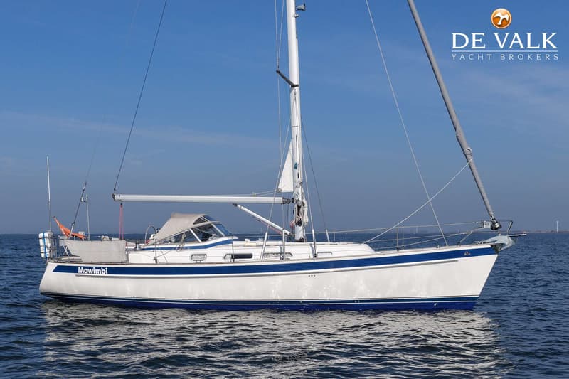 Een witte zeilboot met blauwe strepen en de naam "Mawimbi" op de spiegel, drijft op kalm water onder een heldere lucht.