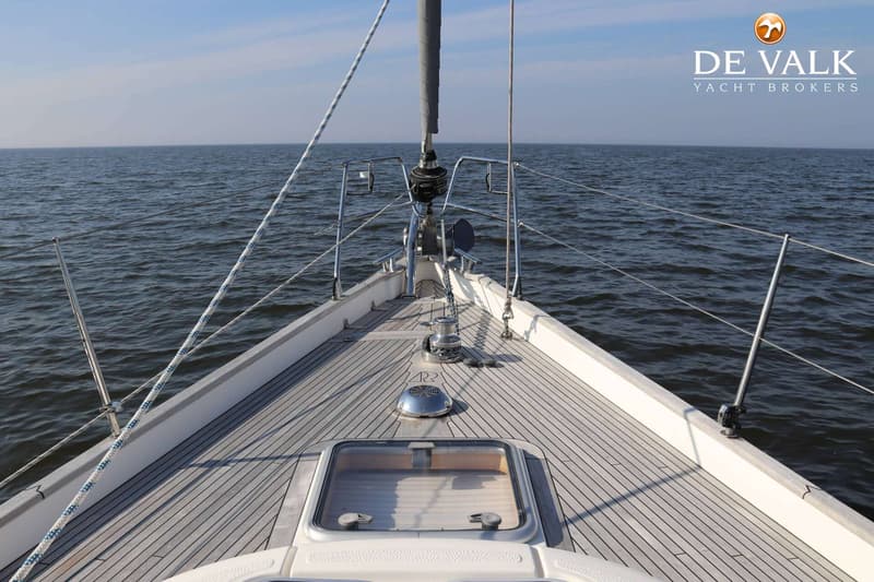 De boeg van een zeilboot met een teakdek, ankerlier, luik en mast, varend op open water. — Hallberg Rassy 40
