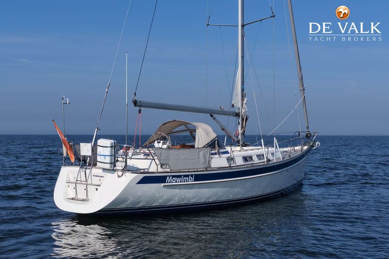 Een witte zeilboot met de naam "Mawimbi" en thuishaven "Hindeloopen" ligt op het water onder een blauwe lucht.