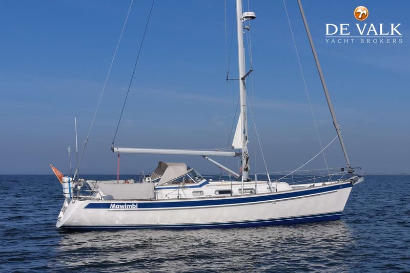 Een witte zeilboot met blauwe strepen en de naam "Mawimbi" op de spiegel, drijft op rustig water onder een heldere blauwe…