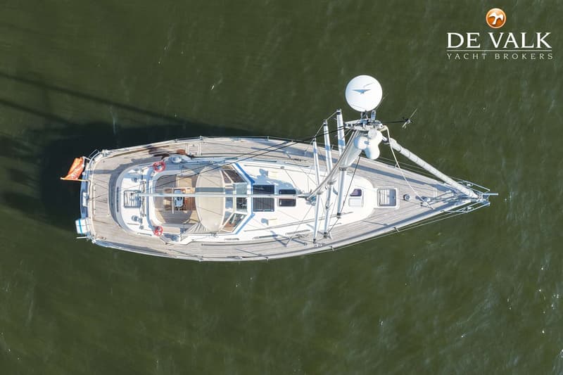 Een zeilboot met houten dek en witte opbouw, gezien van bovenaf op groen water. — Hallberg Rassy 40