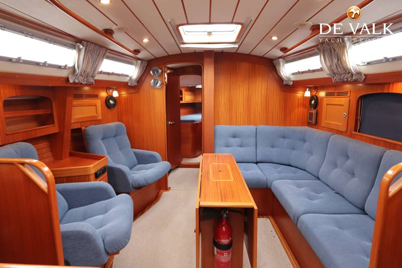 Een interieur van een boot met houten wanden, blauwe zitbanken en stoelen, en een houten tafel met een brandblusser eronder.