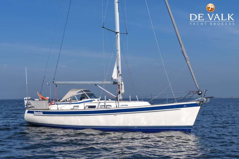 Een witte zeilboot met blauwe strepen en de naam "Mawimbi" op de romp drijft op rustig water. — Hallberg Rassy 40