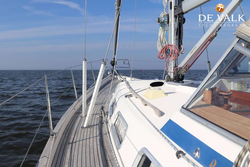Een zeilboot vaart op open water met een blauwe streep op de romp en een houten dek. — Hallberg Rassy 40