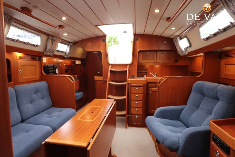 De foto toont het interieur van een boot met houten lambrisering, blauwe banken, een tafel en een kombuis.