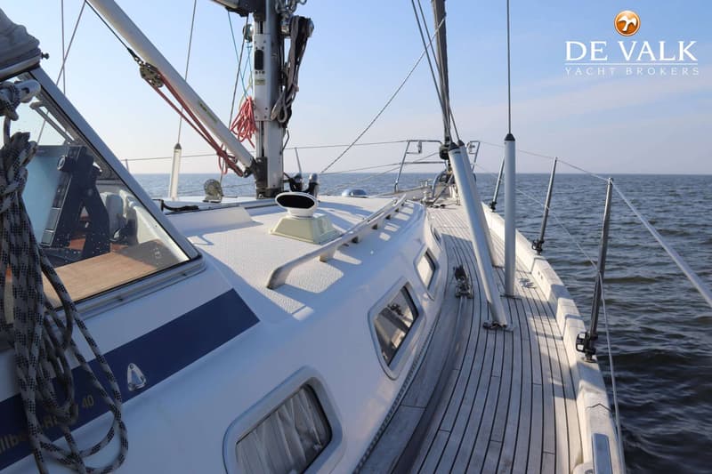 Een bovenaanzicht van het dek van een zeilboot met een witte opbouw, teakhouten dek en de zee op de achtergrond.