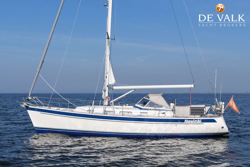 Een witte zeilboot met blauwe strepen en de naam "Mawimbi" vaart op kalm water onder een heldere blauwe lucht.