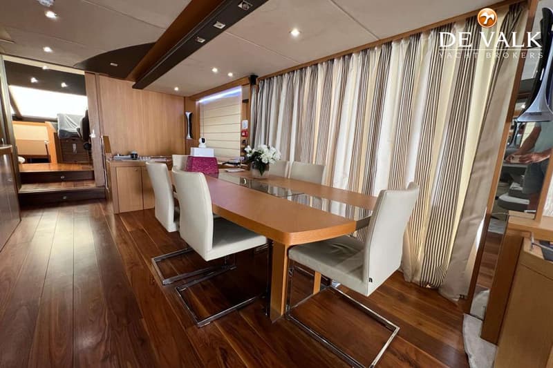 Een houten eettafel met zes stoelen staat in een kajuit met houten vloer en gestreepte gordijnen. — Sunseeker 28 M Yacht
