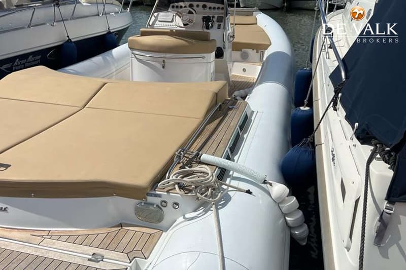 Een witte rubberboot met beige kussens en een teakhouten dek ligt aangemeerd tussen twee andere boten.