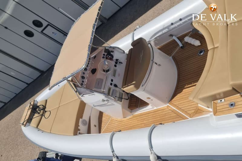 Een bovenaanzicht van een rubberboot met een beige zonnedek, een stuurconsole en een teakhouten vloer.