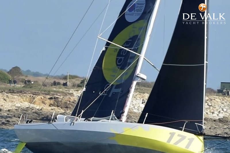 Een zeilboot met nummer 171 en zwarte zeilen met gele opdruk vaart op water langs een rotsachtige kustlijn. — Class 40