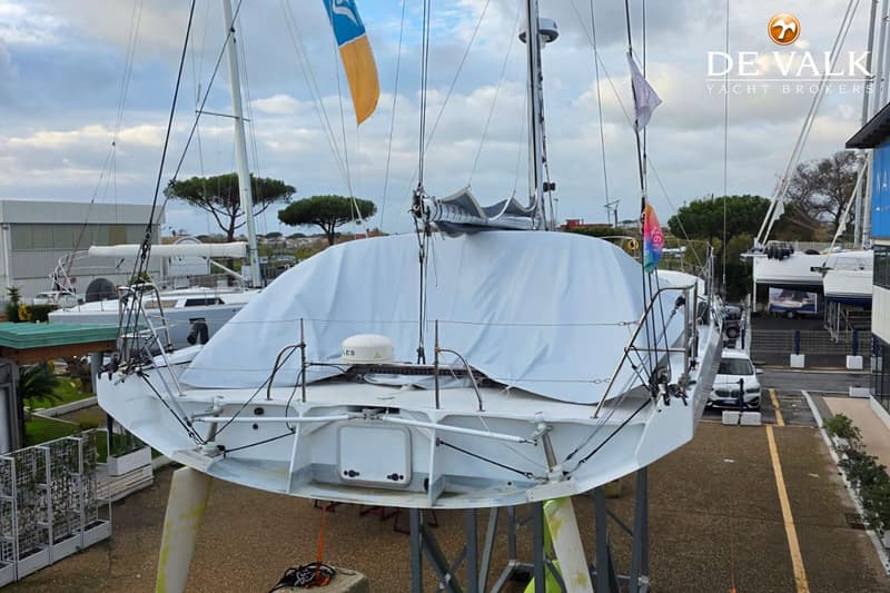 Een zeilboot staat op bokken op de wal, deels afgedekt met een wit zeil, met een De Valk logo rechtsboven. — Class 40