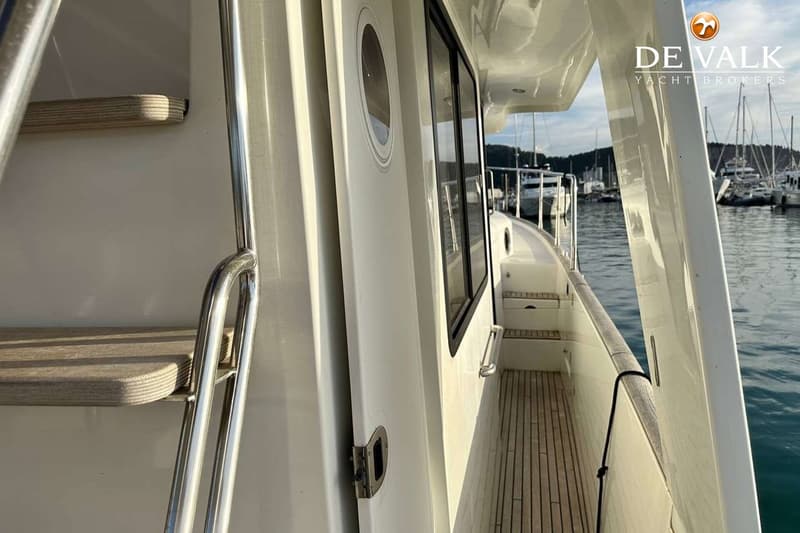 Een witte boot met een teakhouten dek en ramen, met een haven vol boten op de achtergrond. — Beneteau Swift Trawler 44