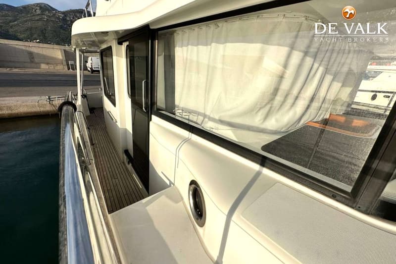 Een witte boot met een teakhouten dek en een schuifdeur, gezien vanaf de zijkant, met een bergachtige kustlijn op de…