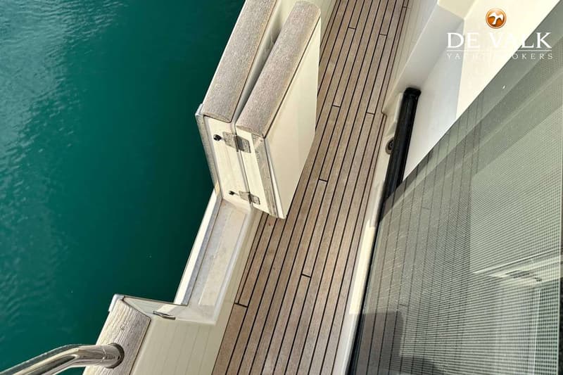 Een teakdek met een opengeklapte bank en een raam met een rasterpatroon, met turquoise water ernaast.
