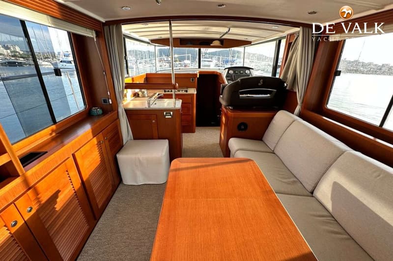 De foto toont het interieur van een boot met een stuurstand, zithoek, tafel en een kombuis. — Beneteau Swift Trawler 44