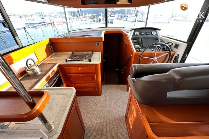 De foto toont het interieur van een boot met een kombuis aan bakboord en een stuurstand aan stuurboord.