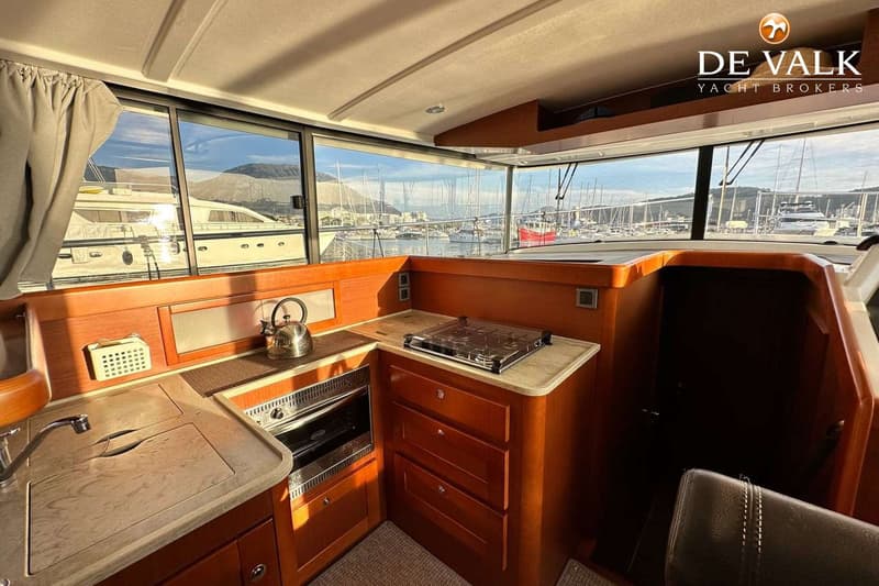 Een interieur van een boot met een kombuis, ramen met uitzicht op een haven en een "DE VALK YACHT BROKERS" logo.