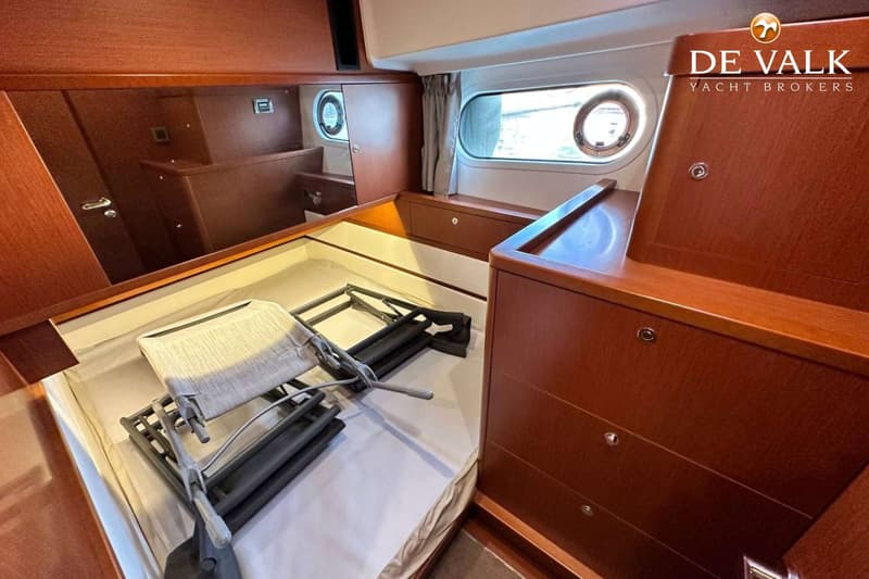 Een kajuit met een bed, houten kasten, een raam met gordijn en patrijspoorten. — Beneteau Swift Trawler 44