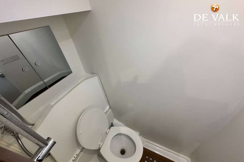 Een witte toiletruimte met een open toiletbril, een spiegelkast en een douchekop.