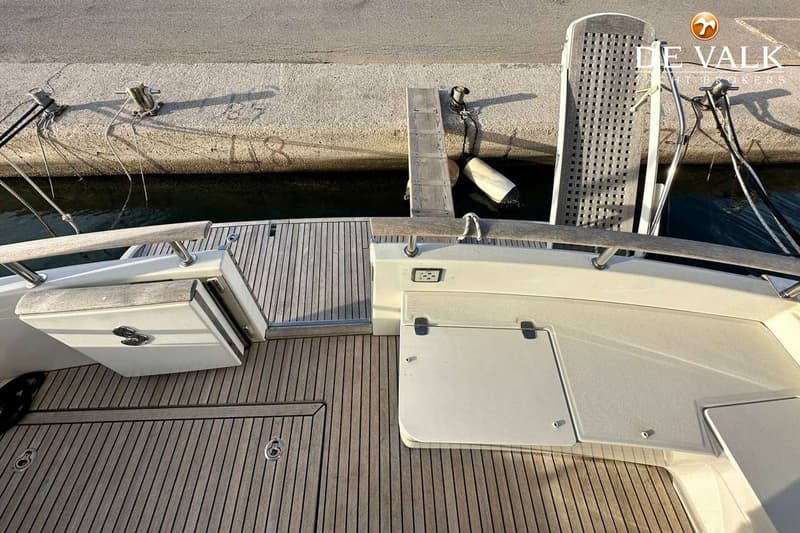 Een bovenaanzicht van het teakhouten dek van een boot, met een open opbergvak en een gesloten luik.