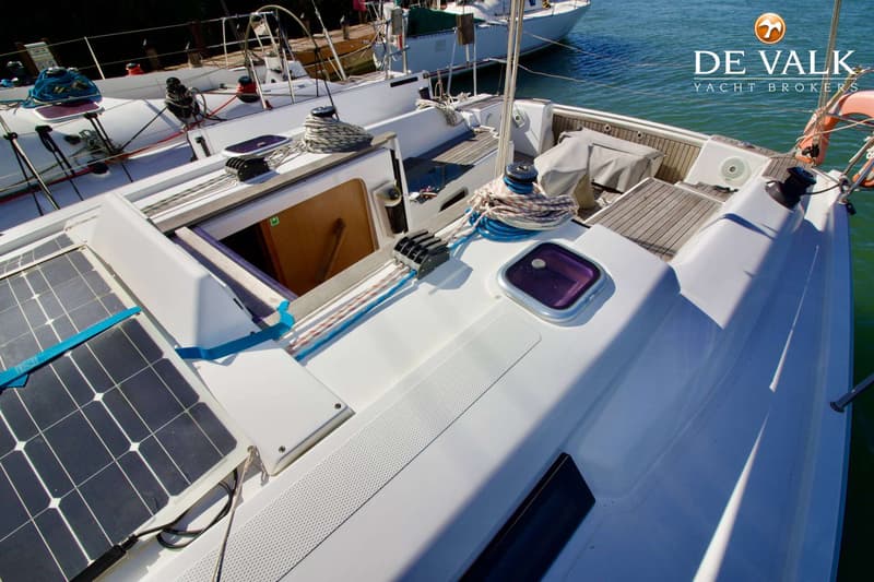 De foto toont het dek van een witte zeilboot met zonnepanelen, touwen, lieren en een open kajuitingang. — Hanse 315