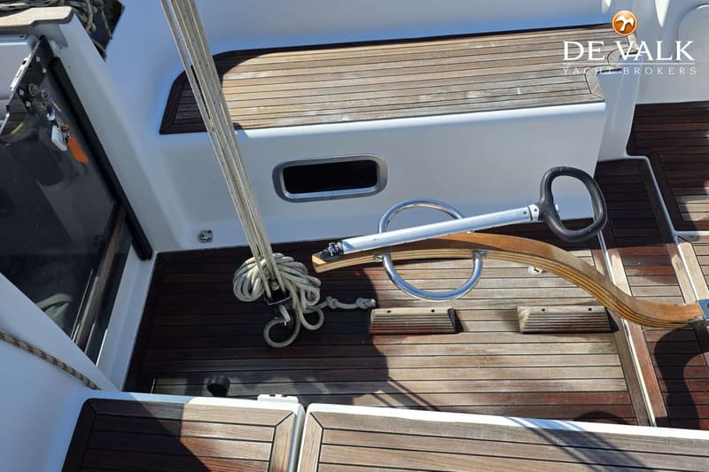 Een dek van een boot met houten latten, een touw opgerold, een roer en een patrijspoort. — Hanse 315