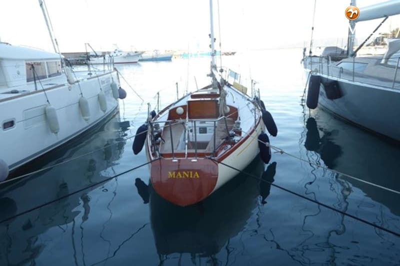 Een zeilboot met de naam "MANIA" op de spiegel ligt afgemeerd tussen twee andere boten in een haven. — Sangermani 10.50