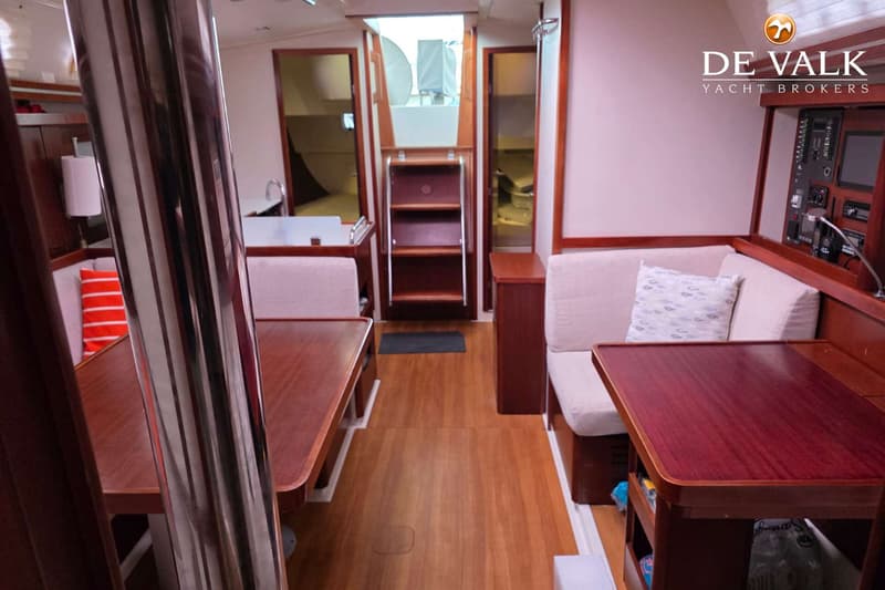 De foto toont het interieur van een boot met houten vloer, twee tafels, banken met kussens, en een trap naar buiten.