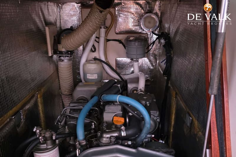 Een detailfoto van een scheepsmotorruimte met een grijze motor, blauwe slangen en isolatiemateriaal op de wanden.