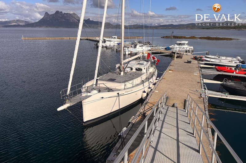 Een zeilboot met de naam "Prospero-Son" ligt afgemeerd aan een steiger, met bergen op de achtergrond. — Puffin 42