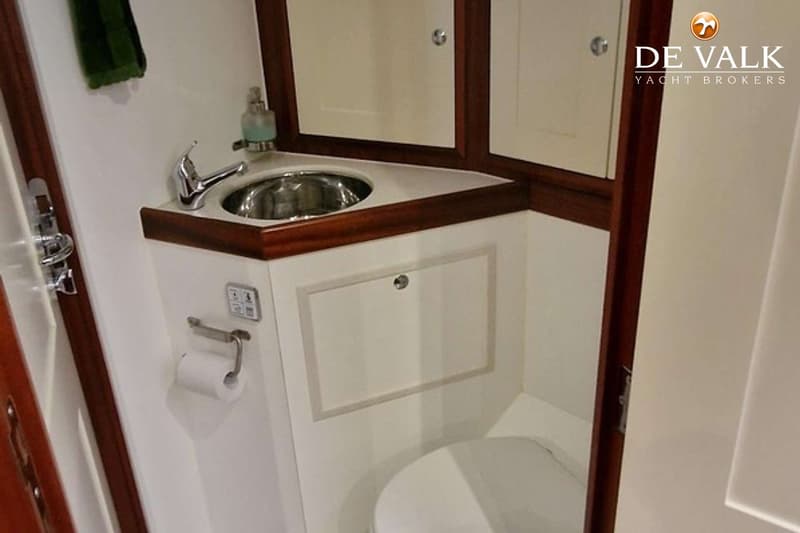 Een badkamer met een wastafel, kraan, zeepdispenser, spiegelkast, toiletrolhouder met toiletpapier en een toilet.