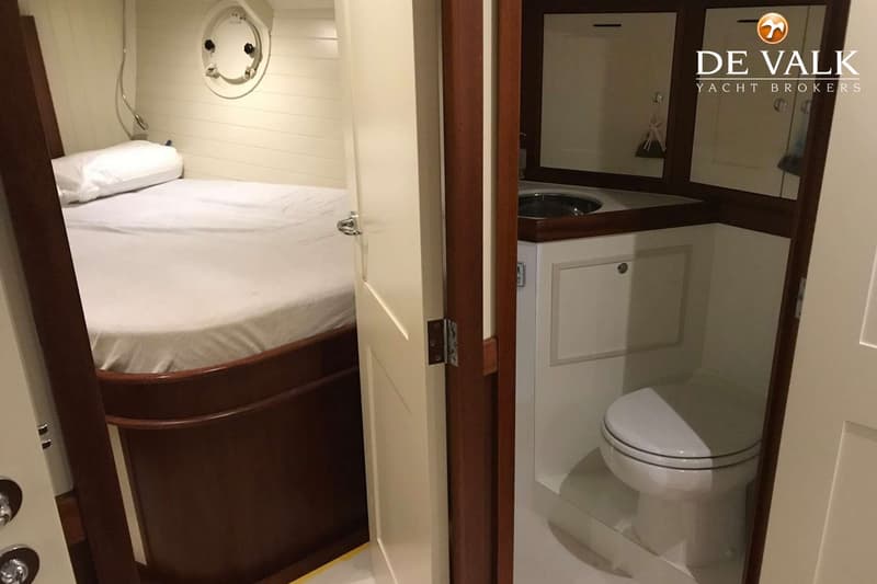 Een slaapkamer met een bed en een patrijspoort, en een badkamer met een toilet en wastafel.