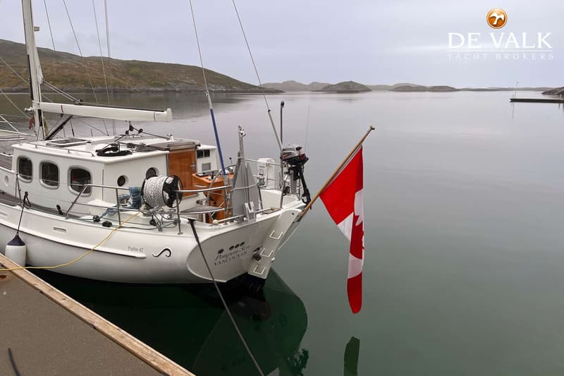 Een witte zeilboot met een Canadese vlag aan de achtersteven ligt aangemeerd aan een houten steiger. — Puffin 42