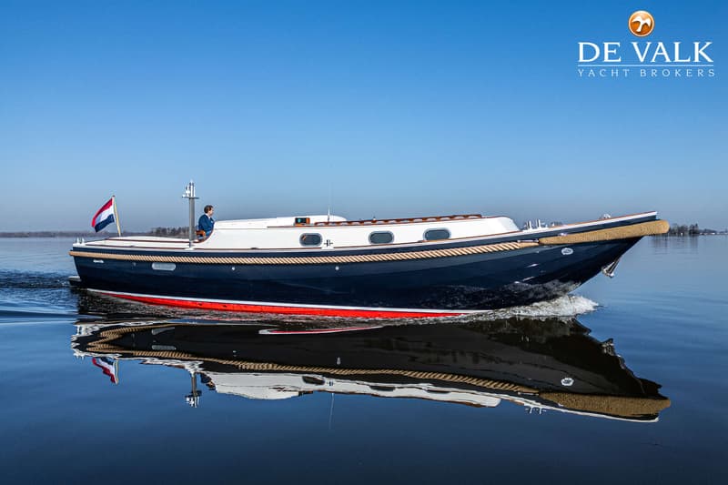 Een donkerblauwe boot met een witte opbouw en een rode waterlijn vaart op rustig water onder een heldere blauwe lucht.