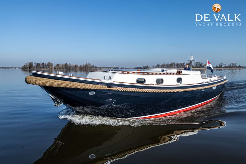 Een donkerblauwe boot met witte opbouw en een touwstootrand vaart op kalm water onder een helderblauwe lucht.
