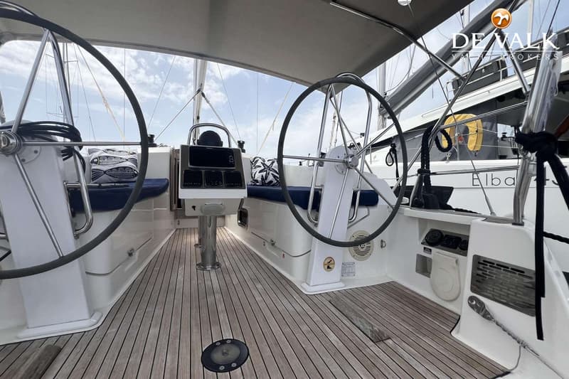 De foto toont de kuip van een zeilboot met twee stuurwielen, een houten dek en blauwe kussens. — Bavaria Cruiser 37