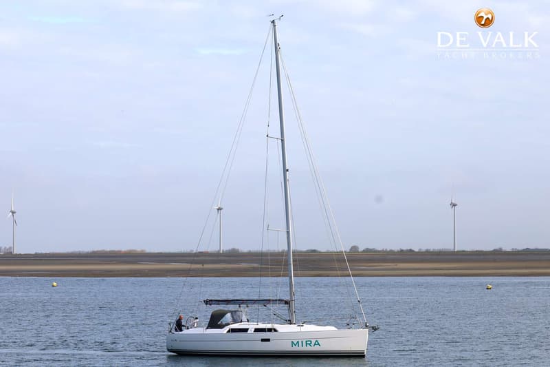 Een witte zeilboot met de naam "MIRA" vaart op water met windmolens op de achtergrond. — Hanse 375