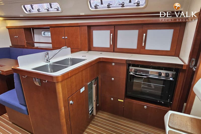 De foto toont een scheepskeuken met een dubbele spoelbak, een kraan, een fornuis met oven en een koelkast.