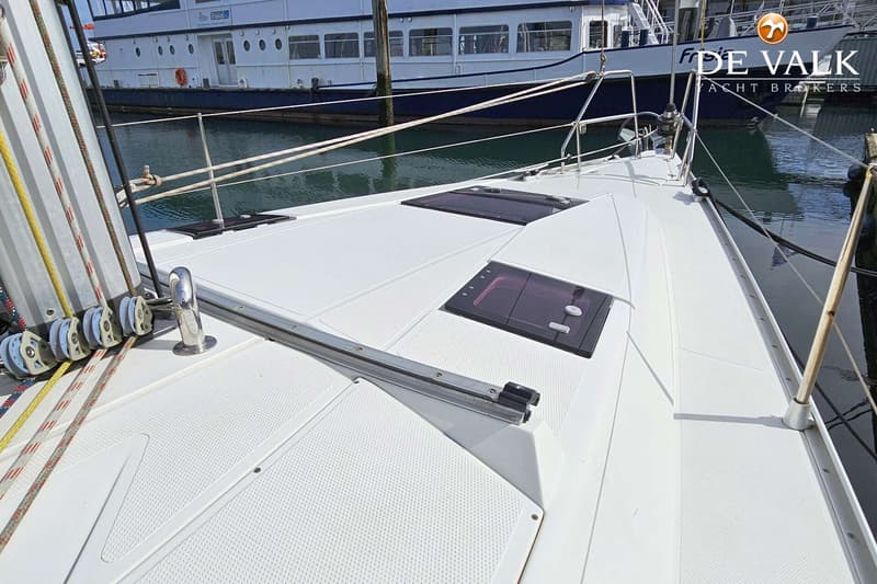 Een wit dek van een zeilboot met luiken en lijnen, met een ander schip en water op de achtergrond. — Hanse 375