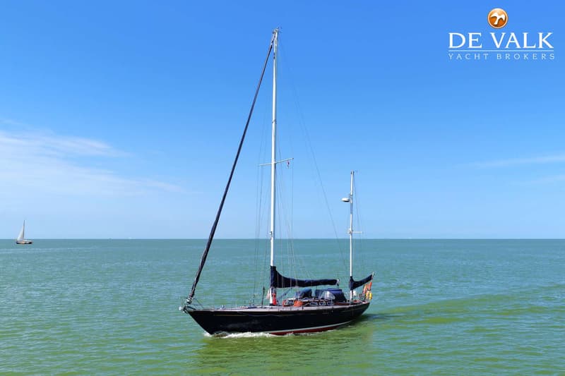 Een donkerblauwe zeilboot met twee masten vaart op groen water onder een helderblauwe lucht. — Huisman 45